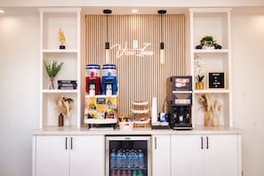 A beverage station with multiple dispensers, a refrigerator stocked with bottled water, and a welcome sign. - Viva Inn (Houston)