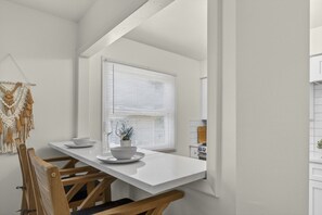 A dining area with a white table, two chairs, and a window with blinds. - Cozy Stylish Apt in Omaha`s Medical District! (Omaha)