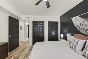A bedroom with a bed, a nightstand, a lamp, and a wall-mounted light fixture. - Cozy Stylish Apt in Omaha`s Medical District! (Omaha)