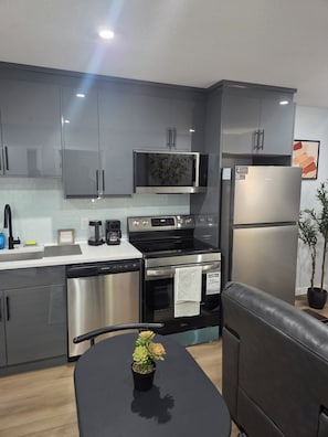 A modern kitchen with grey cabinets, a stainless steel refrigerator, a microwave, and a stove. - Cozy Private 1-Bedroom Suite |  Free Parking & Wi-Fi (Regina)