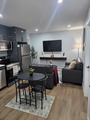 A modern kitchen with a dining area, a flat-screen TV, and a sofa. - Cozy Private 1-Bedroom Suite |  Free Parking & Wi-Fi (Regina)