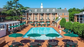 A hotel with a central swimming pool surrounded by outdoor seating and umbrellas.