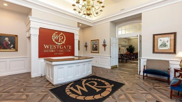 Een receptiegedeelte met een bord voor Westgate Historic Williamsburg Resort, een kroonluchter, ingelijste kunstwerken en een kamerbreed tapijt met dessin.
