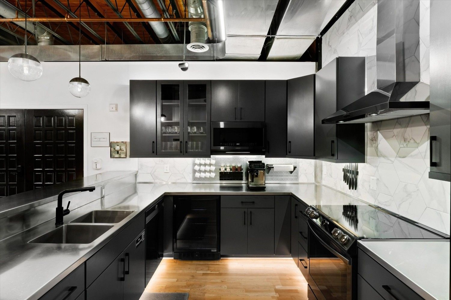 A modern kitchen with black cabinets, a stainless steel sink, and a marble backsplash.