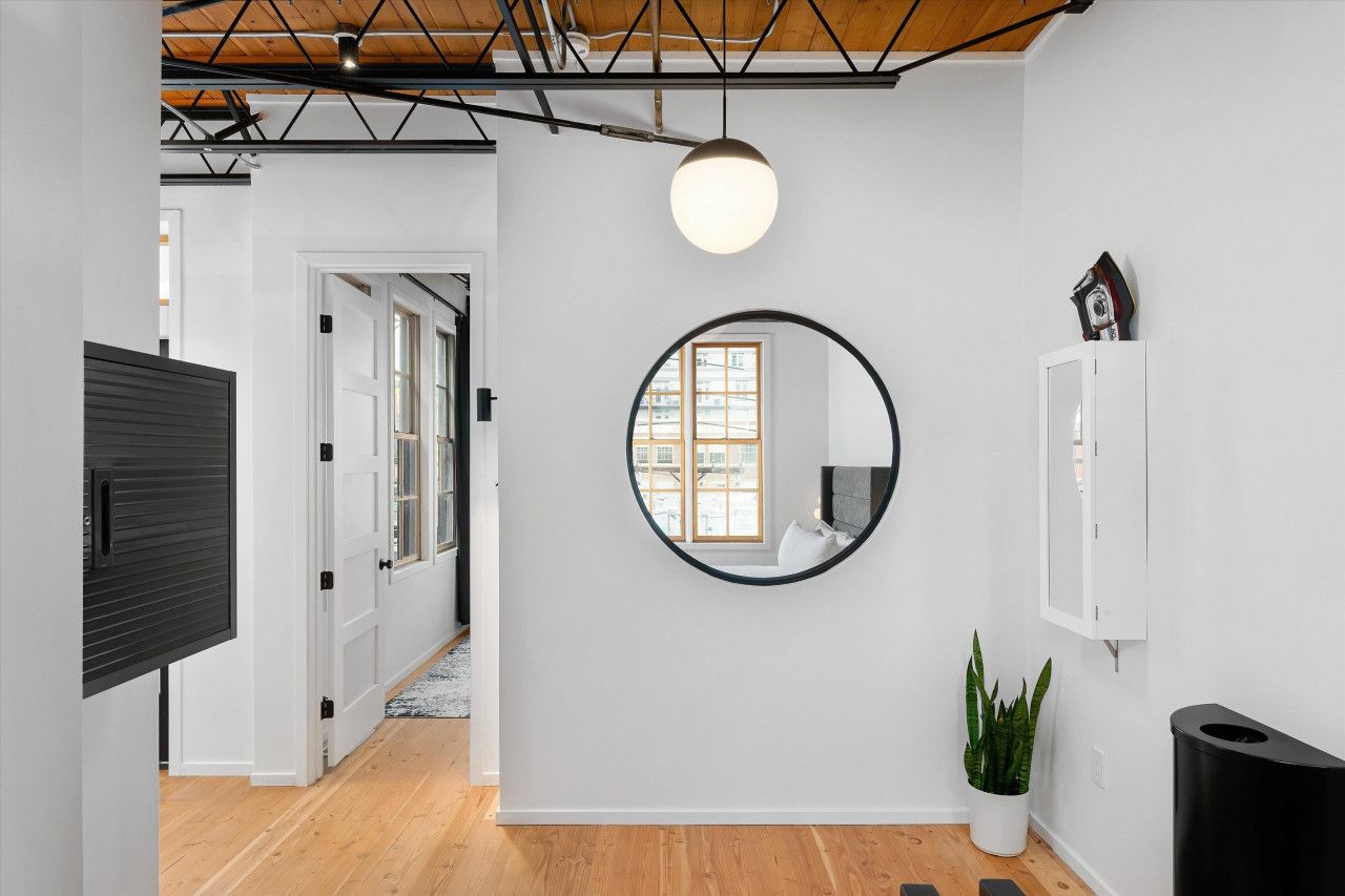 A hallway with a round mirror on the wall, a potted plant, and a black trash bin.