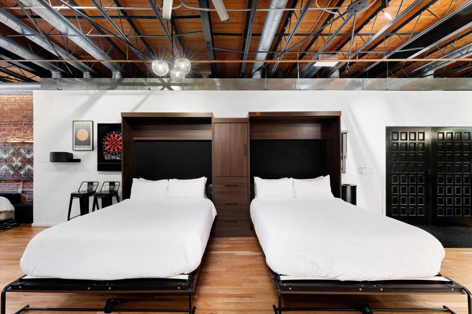 Une chambre d’hôtel avec deux lits, un mur en briques et un plafond avec des poutres apparentes.