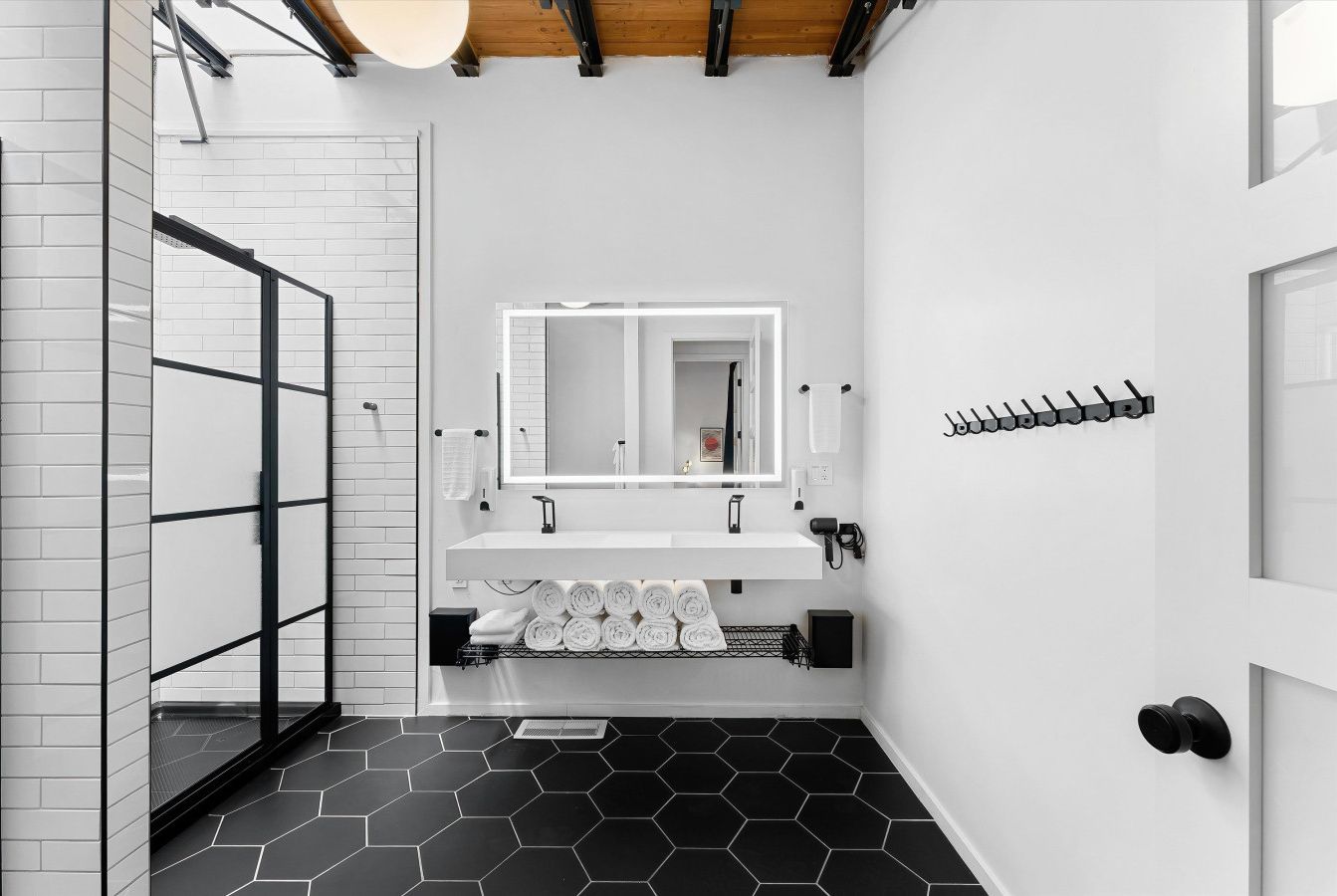 A modern bathroom with a white sink, black hexagonal tiles, a glass shower enclosure, and a towel rack.