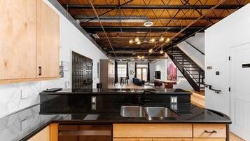A modern kitchen with a black countertop, wooden cabinets, and a visible staircase leading to another level.