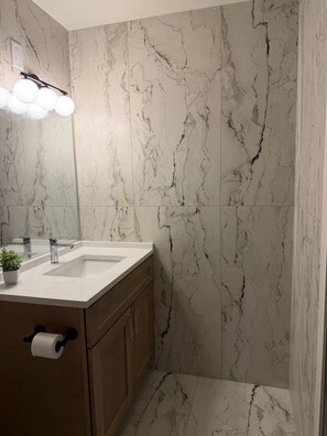 A bathroom with a marble wall, a sink with a mirror, and a toilet. - Cozy Stylish Apt in Omaha`s Medical District! (Omaha)