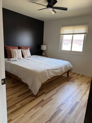 A bedroom with a bed, a ceiling fan, a window with blinds, and a nightstand with a lamp. - Cozy Stylish Apt in Omaha`s Medical District! (Omaha)