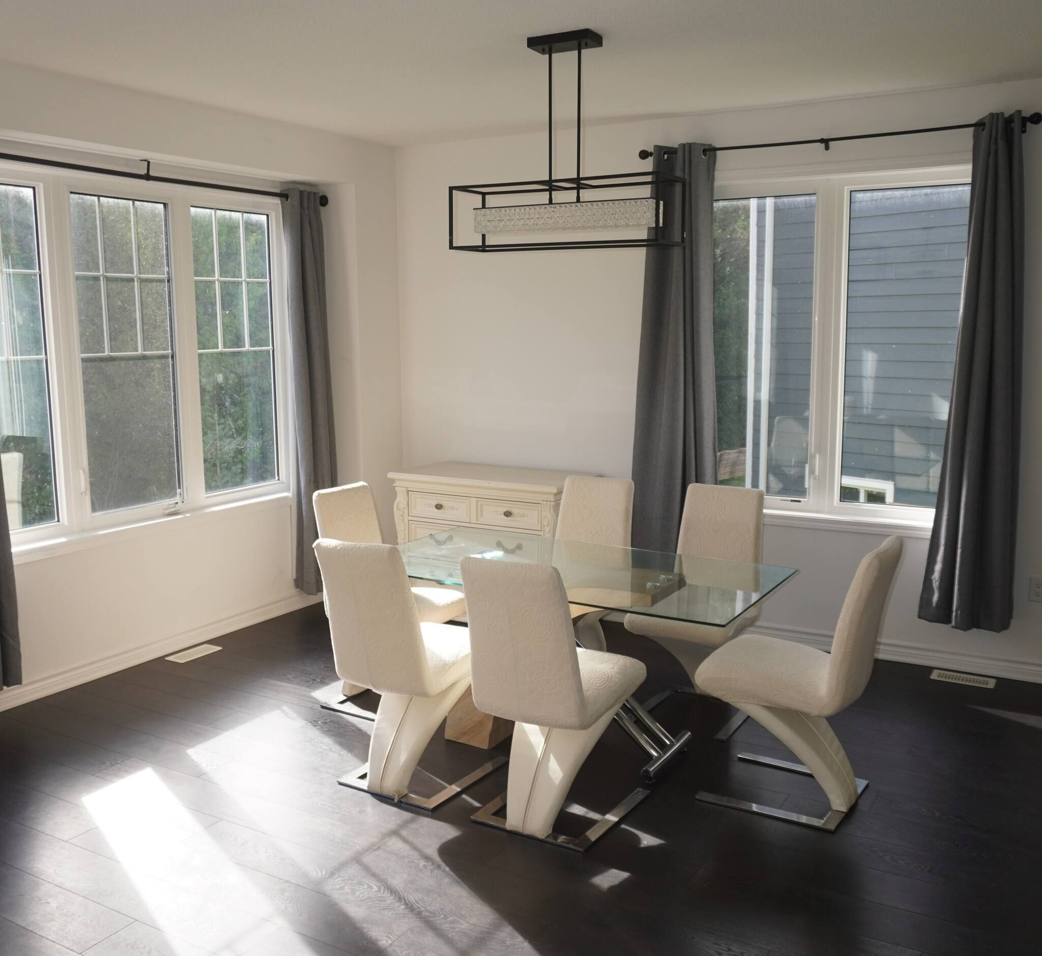 A dining area with a glass table surrounded by chairs, a white cabinet, and a pendant light.