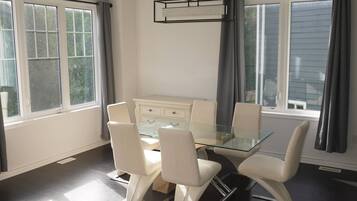 A dining area with a glass table surrounded by chairs, a white cabinet, and a pendant light.