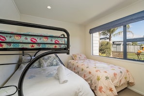 A bunk bed with patterned bedding, a window with a view of the outdoors, and a ceiling light. - The Holiday Hideaway - Pauanui Holiday Home (Pauanui)