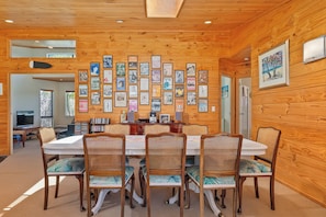 A dining area with a wooden ceiling, a wall adorned with framed posters, and a table set with chairs. - The Holiday Hideaway - Pauanui Holiday Home (Pauanui)