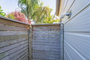 Une porte en bois mène à une cour arrière où se trouve une maison au revêtement blanc et un palmier.