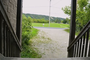 A view through a wooden gate leading to a paved path with a grassy area and a sports field in the distance. - Blue Mountains Chalet | Sleeps 18 | Hot Tub & BBQ I 1 Minute Drive to Village (The Blue Mountains)