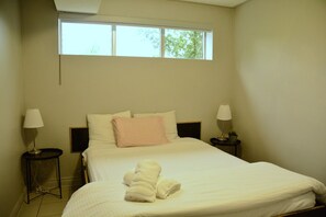 Una habitación de hotel con una cama, dos lámparas de noche, un ventanal y una mesita con una planta.