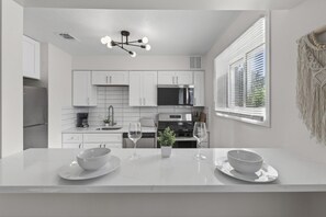 A modern kitchen with white cabinetry, a central island with two bowls and wine glasses, and a pendant light. - Cozy Stylish Apt in Omaha`s Medical District! (Omaha)