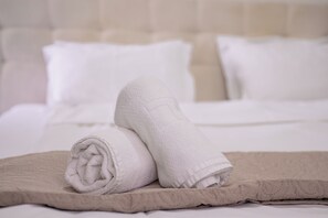 A neatly made bed with white linens and a rolled towel on a beige bed runner. - Astera Apart Hotel -Cozy studio with AC in gorgeous Skopje perfect for your stay (Skopje)