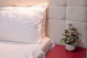 A bed with white bedding, a red nightstand, and a potted plant with variegated leaves. - Astera Apart Hotel -Cozy studio with AC in gorgeous Skopje perfect for your stay (Skopje)