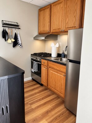 A modern kitchen with wooden cabinets, a stainless steel refrigerator, and a gas stove. - Modern 1BR Cottage Retreat Near College (Swarthmore)