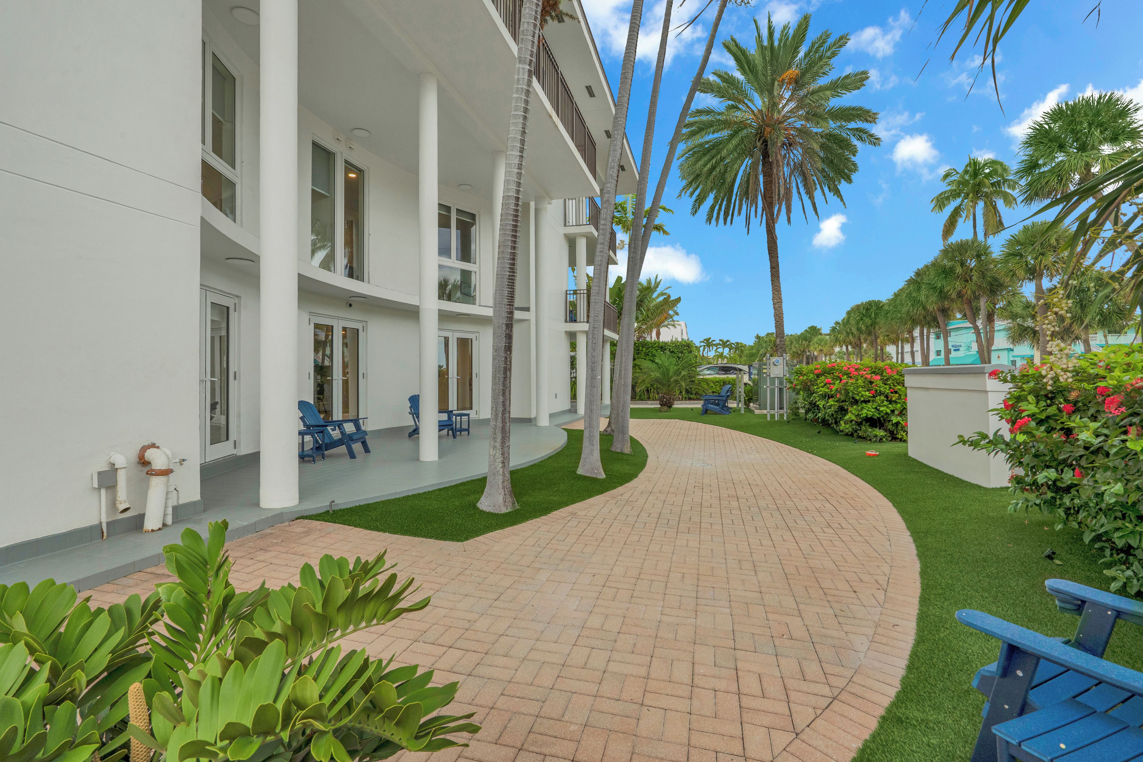 A hotel with a curved brick pathway, palm trees, and outdoor seating.
