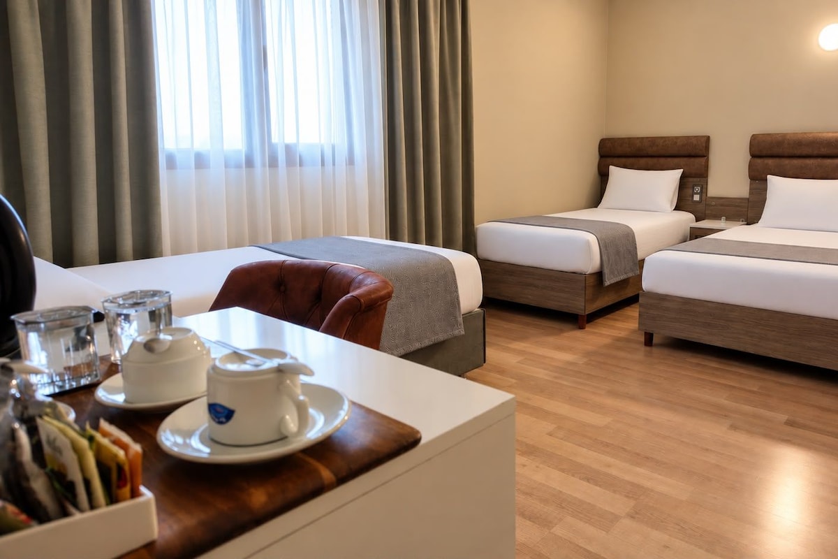 Una camera d'albergo con due letti, una scrivania con una sedia e un tavolo con teiera e tazze.