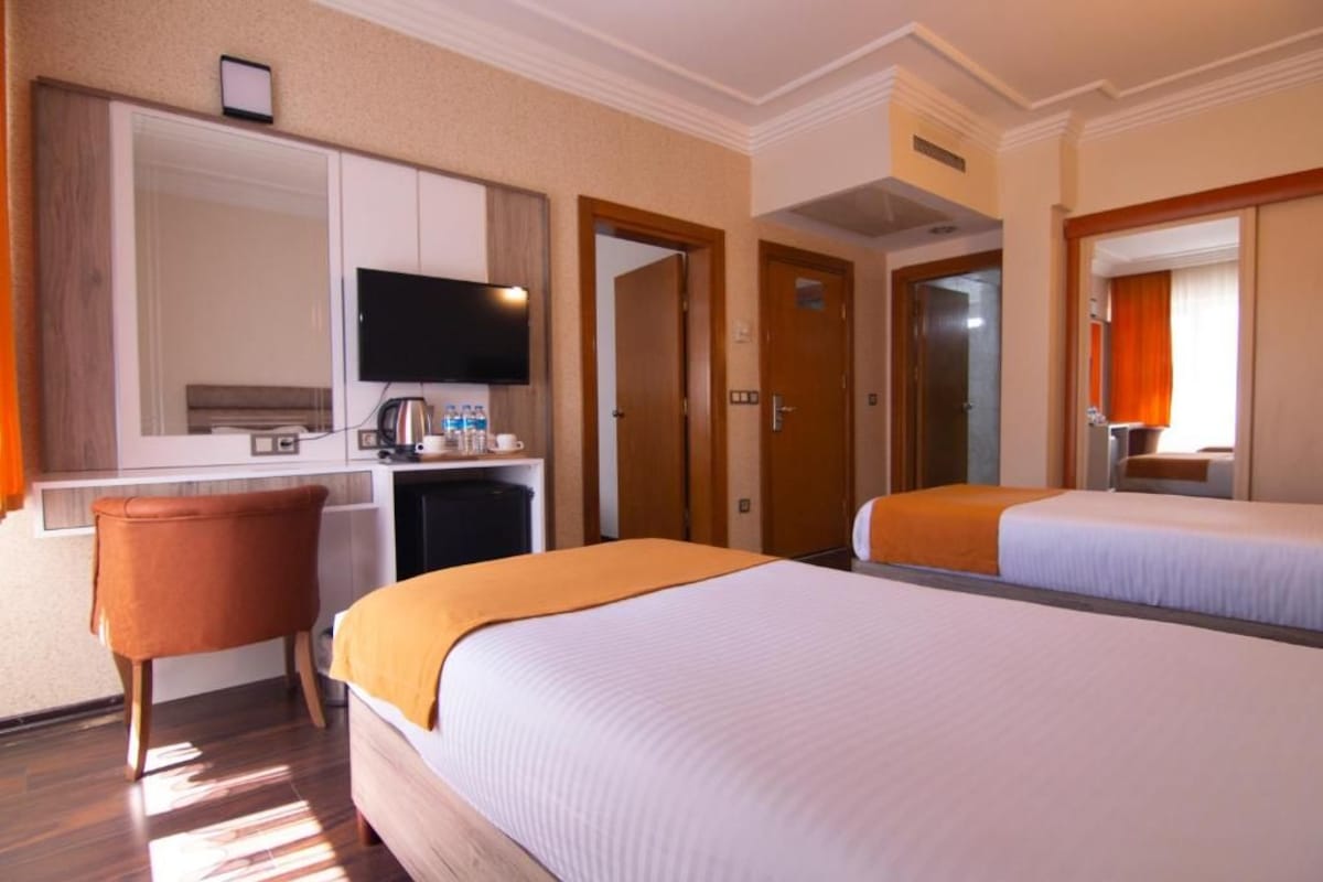 Una camera d'albergo con due letti, una scrivania con televisore e un piccolo angolo salotto.