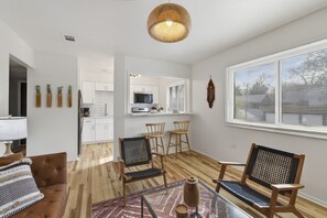 A modern living room with a sofa, two chairs, a glass coffee table, and a kitchen area with white cabinets and a microwave. - Cozy Stylish Apt in Omaha`s Medical District! (Omaha)