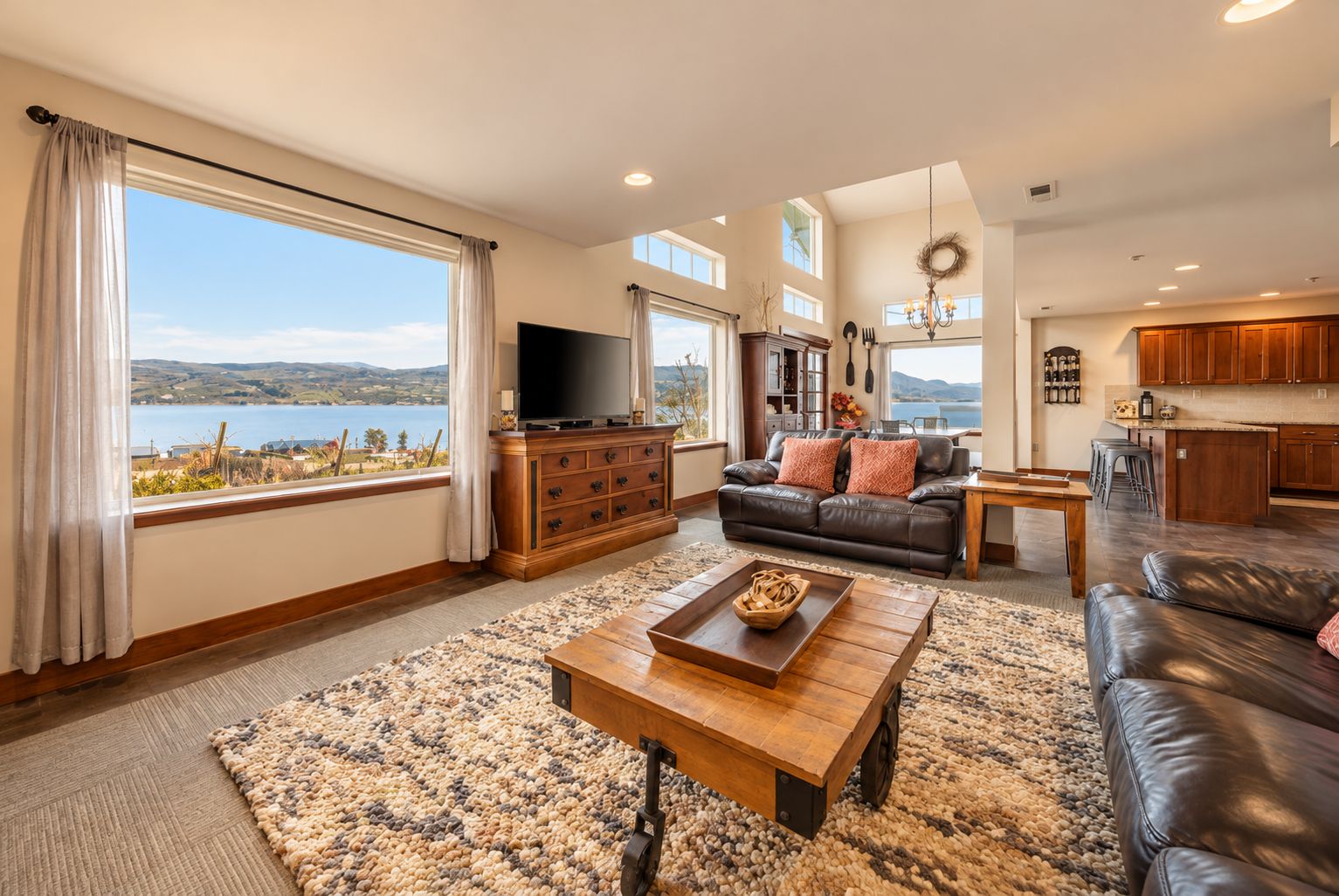 A spacious living room with a large window, a flat-screen TV, a leather sofa, and a wooden coffee table.