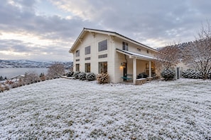 Une maison à deux étages avec un porche abrité, une vue sur un lac et un sol recouvert de neige.