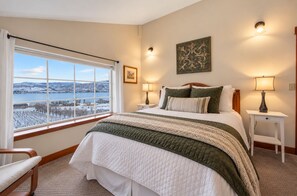 Une chambre avec un grand lit, une fenêtre donnant sur un paysage enneigé, une table de chevet avec une lampe et un luminaire fixé au mur.