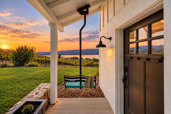 Un espacio al aire libre cubierto con un banco, una puerta y vistas a un viñedo al atardecer.