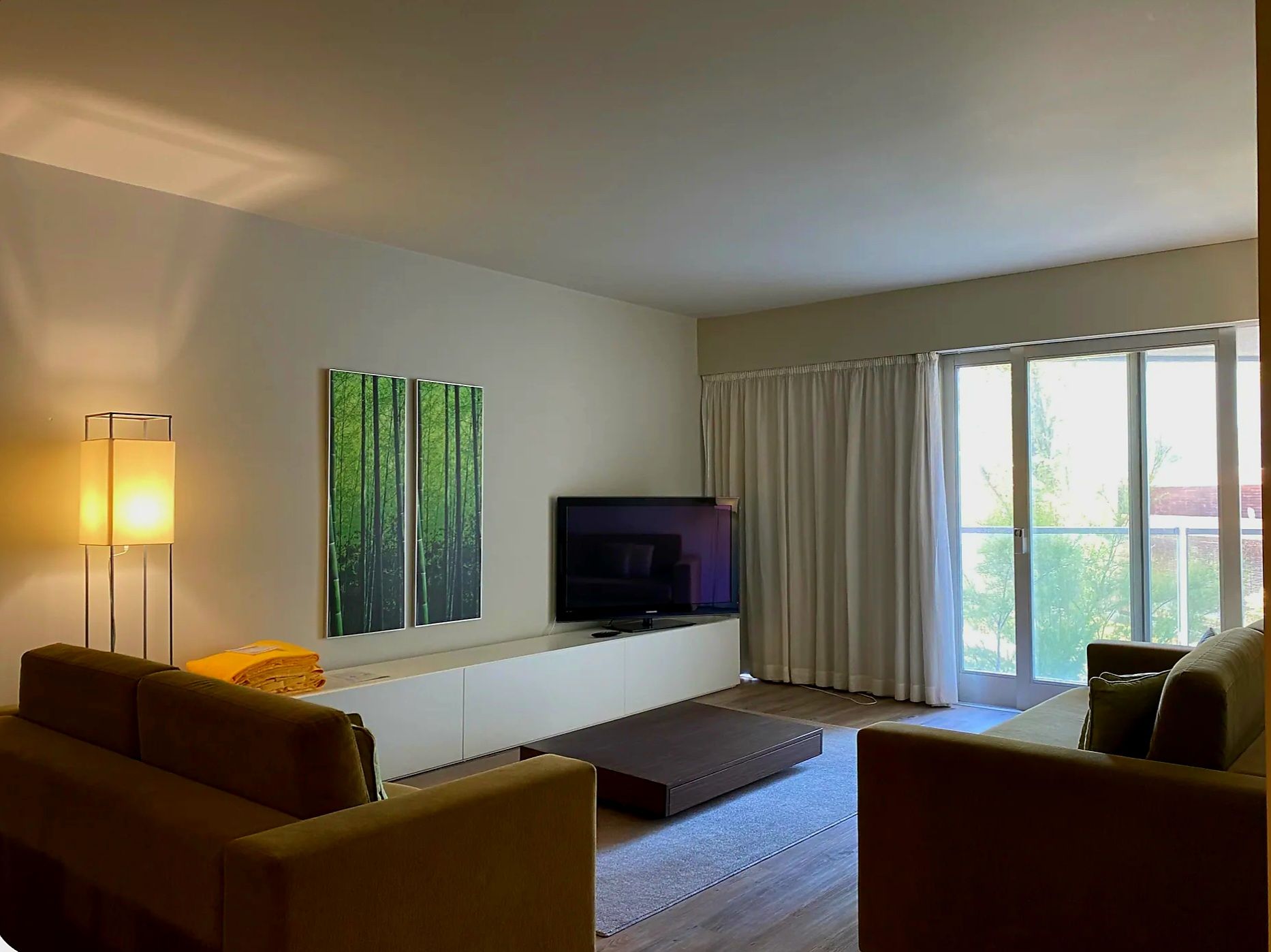 Una sala de estar moderna con un televisor de pantalla plana, dos cuadros colgados en la pared, una lámpara de pie y un sofá.