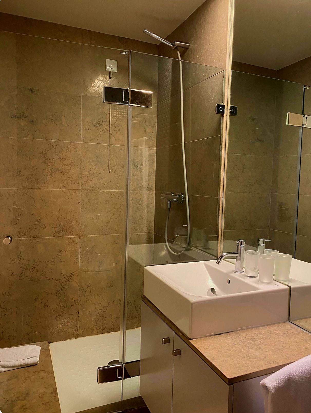 A bathroom with a glass-enclosed shower, a white sink, and a mirror.