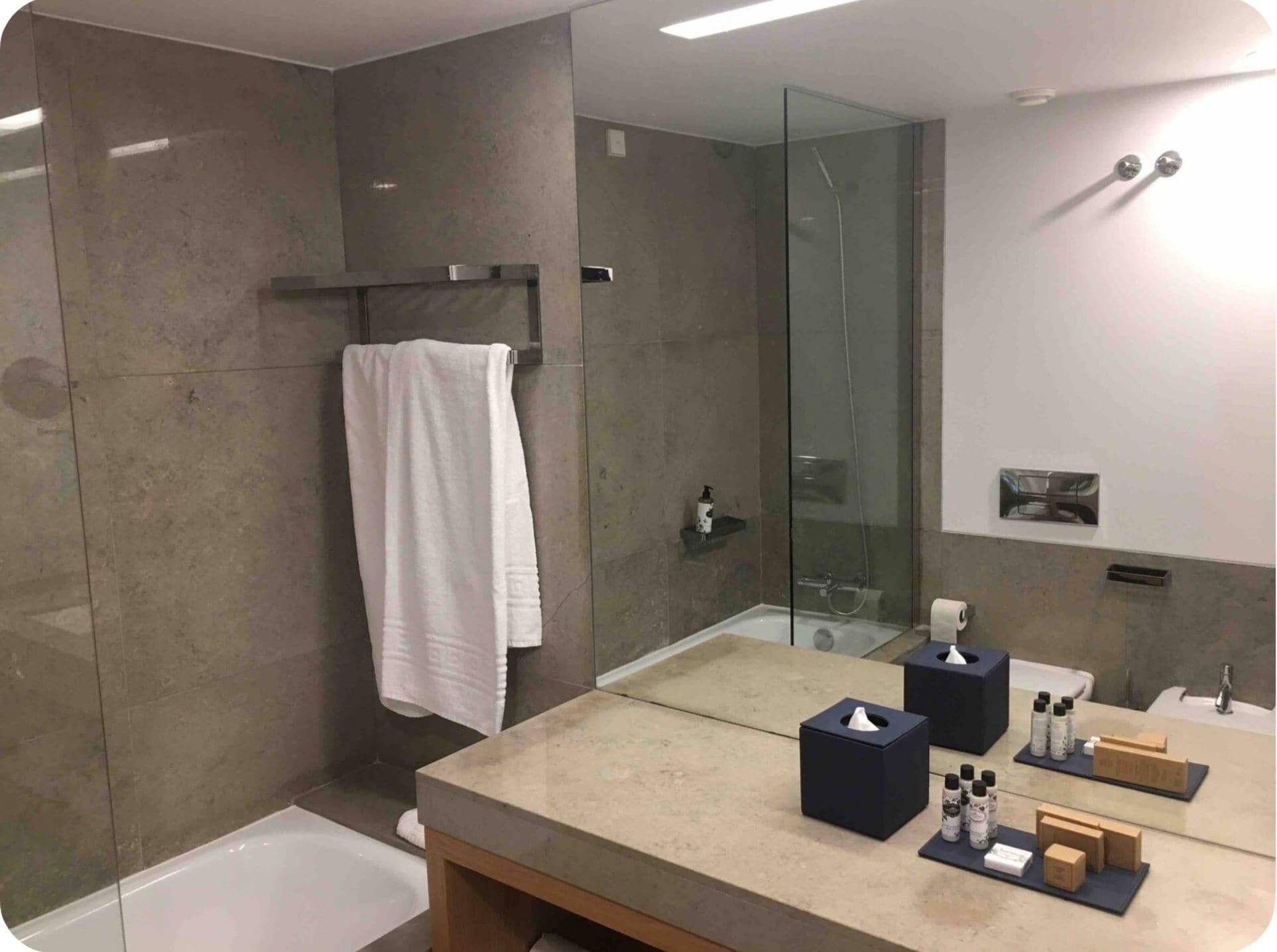 A modern bathroom with a glass shower enclosure, a large mirror, and a vanity with toiletries.
