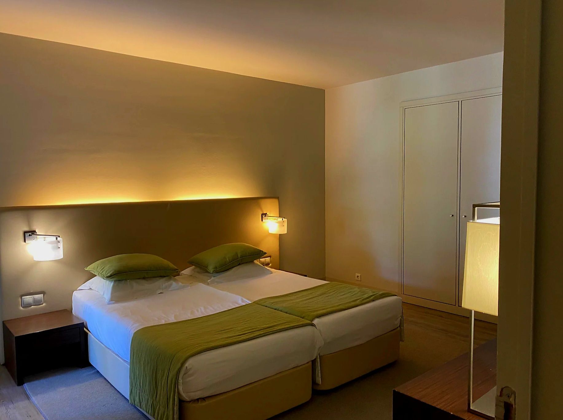 A hotel room with a bed, bedside lamps, a nightstand, and a wardrobe.
