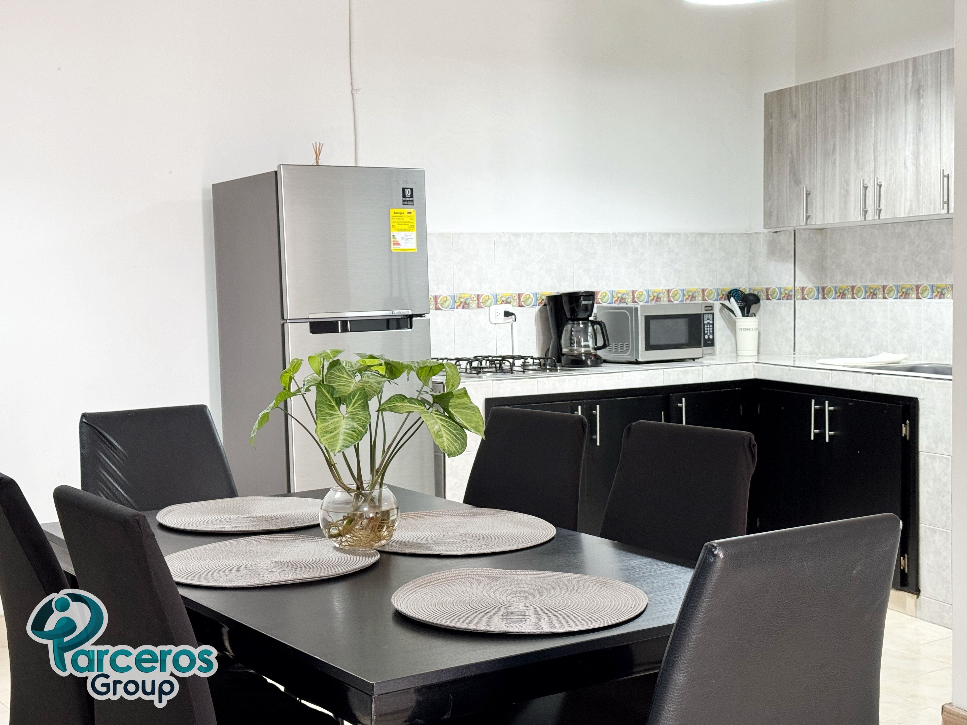 Cocina moderna con refrigerador, microondas y estufa. Hay una mesa de comedor con sillas y un florero con plantas.