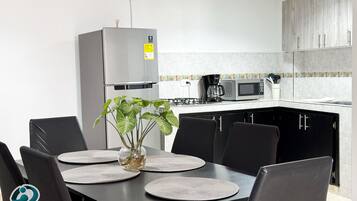 Cocina moderna con refrigerador, microondas y estufa. Hay una mesa de comedor con sillas y un florero con plantas.