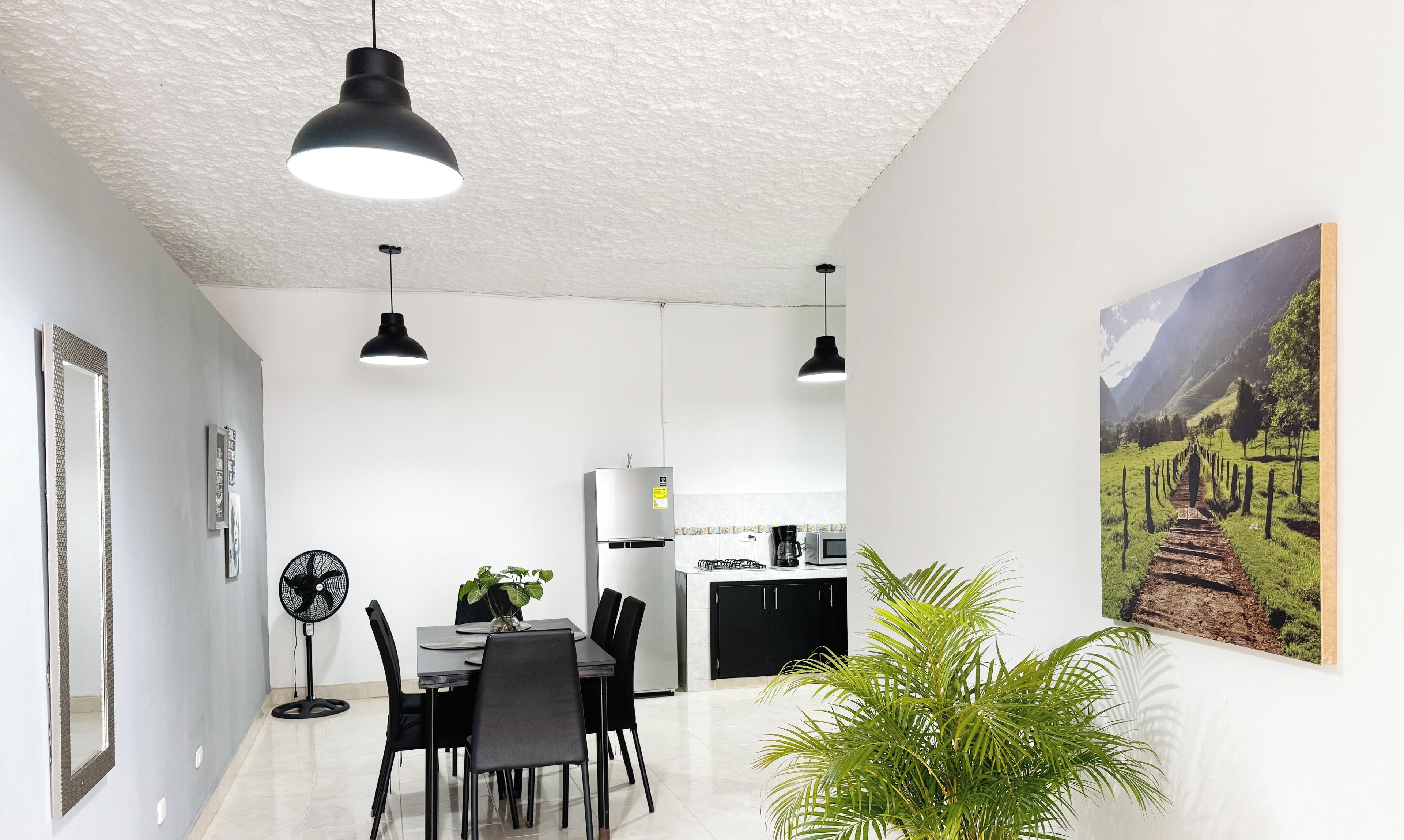 A modern kitchen with a refrigerator, microwave, and coffee maker. There is a dining area with a table and chairs, and a potted plant.