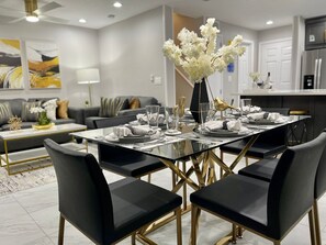 A modern dining area with a glass table set for six, black upholstered chairs, and a vase with white flowers. - Fantasy World Resort, The Lego House - Free Waterpark and free Disney Shuttle (Kissimmee)