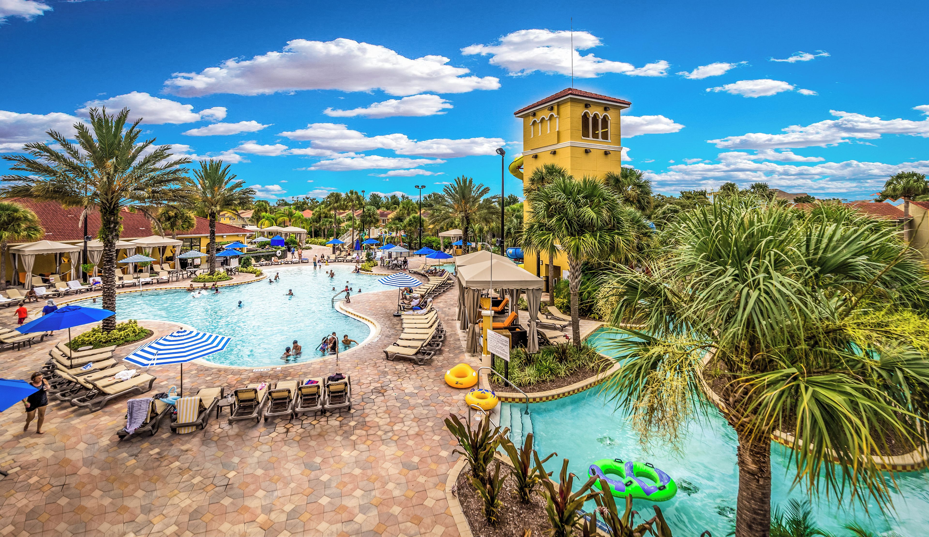 A resort pool area with multiple pools, lounge chairs, umbrellas, and palm trees.
