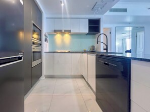 A modern kitchen with stainless steel appliances, a dishwasher, and a countertop with a sink. - Azure 41 Level 41 Ocean Views, Surfers (Surfers Paradise)