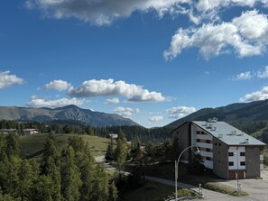 A mountain landscape with a building featuring a sloped roof and a small parking area. - Bel appartement avec terrasse et garage - vue pistes (Péone)