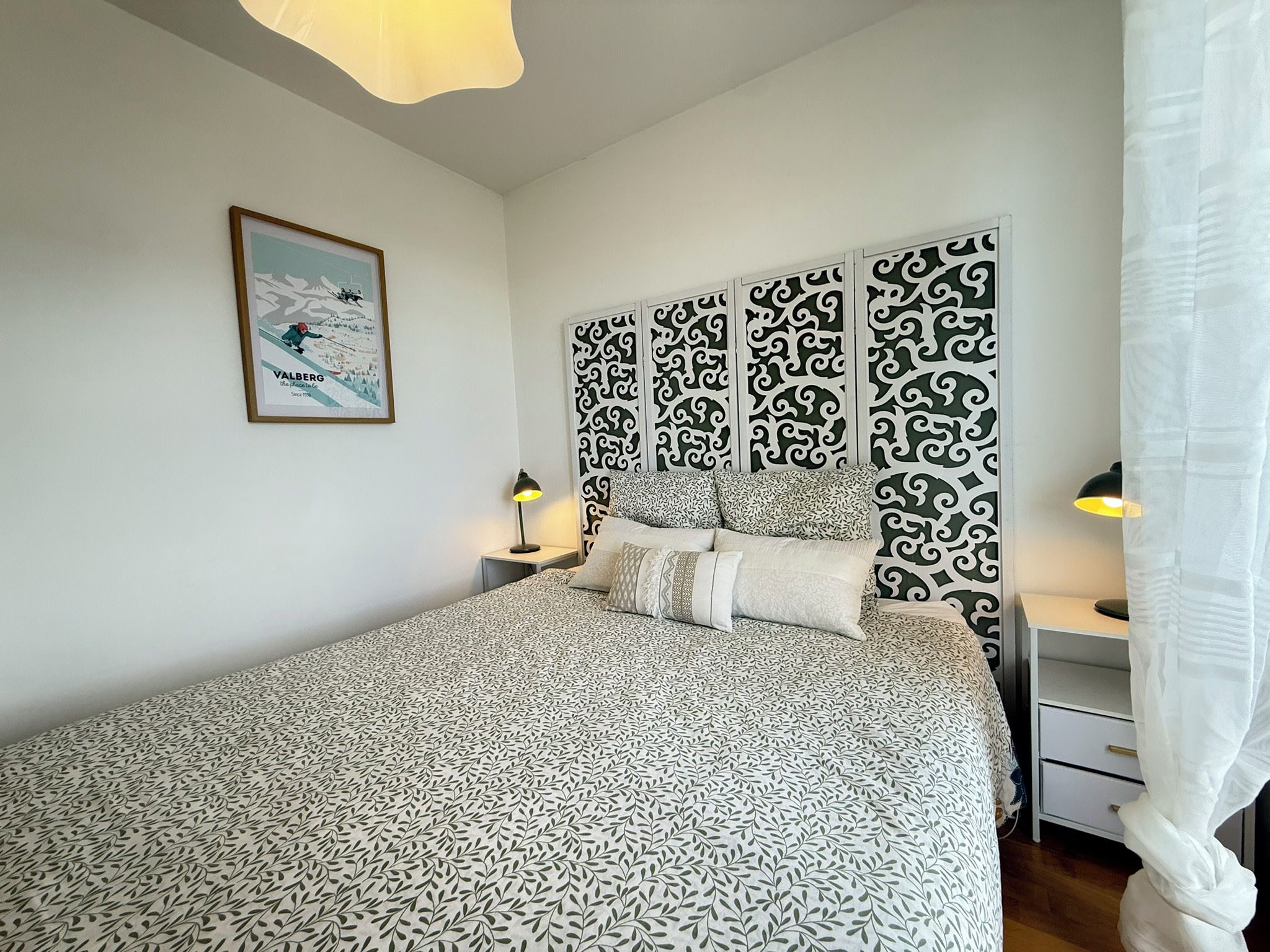 A bedroom with a bed, a nightstand, a lamp, a framed picture, and a decorative wall panel.