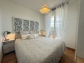 A bedroom with a large bed, a nightstand, a lamp, a decorative headboard, and a view through a window. - Bel appartement avec terrasse et garage - vue pistes (Péone)