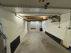 A narrow hallway with a concrete floor, white walls, and a ceiling with exposed beams and fluorescent lighting. - Bel appartement avec terrasse et garage - vue pistes (Péone)