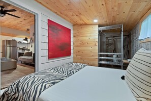 Ein Schlafzimmer mit einem Bett, einem roten Kunstwerk, einem Kleiderschrank und einem durch eine offene Tür einsehbaren Küchenbereich.