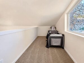 A corner room with a window, a crib, and a carpeted floor. - Spacious Midtown Home, Walk to Lake & Downtown (Coeur d'Alene)