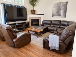 A living room with a brown leather sofa, a flat-screen TV, a fireplace, and a framed picture on the wall. - Spacious Midtown Home, Walk to Lake & Downtown (Coeur d'Alene)